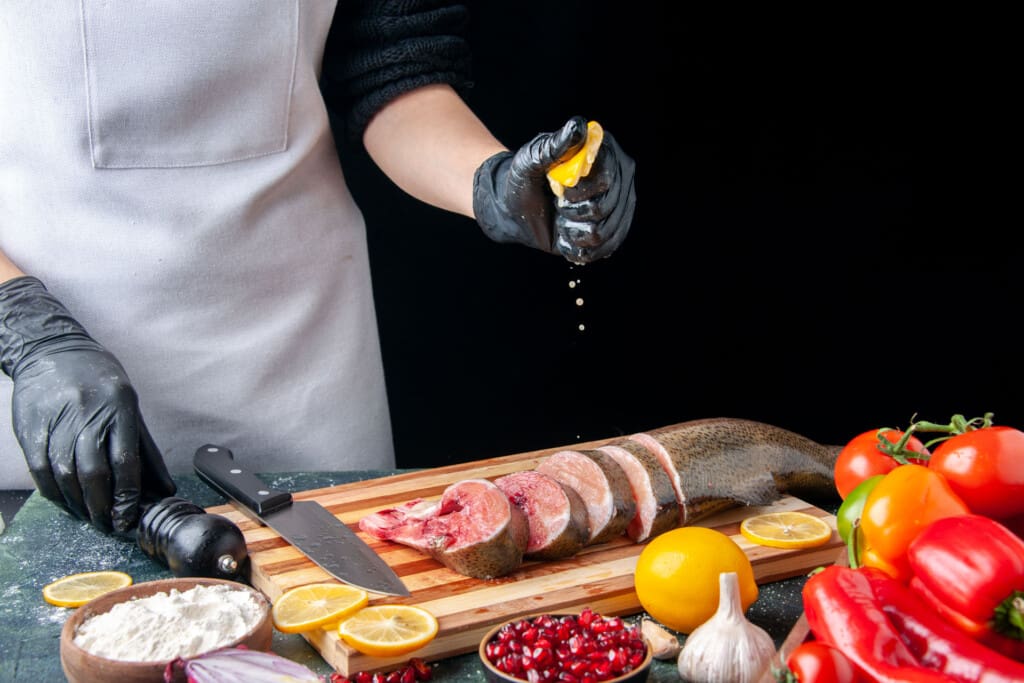 front view chef squeezing lemon raw fish slices knife cutting board vegetables wood serving board kitchen table