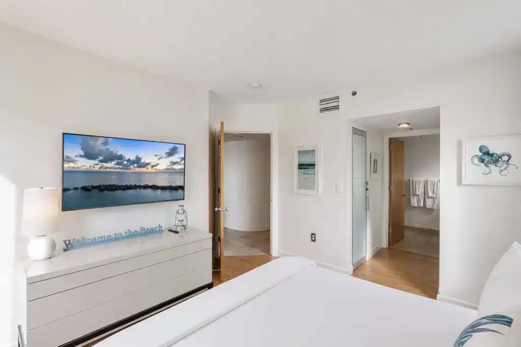Modern Miami bedroom with flat-screen TV, white dresser, and ensuite bathroom in Retreats Miami rental