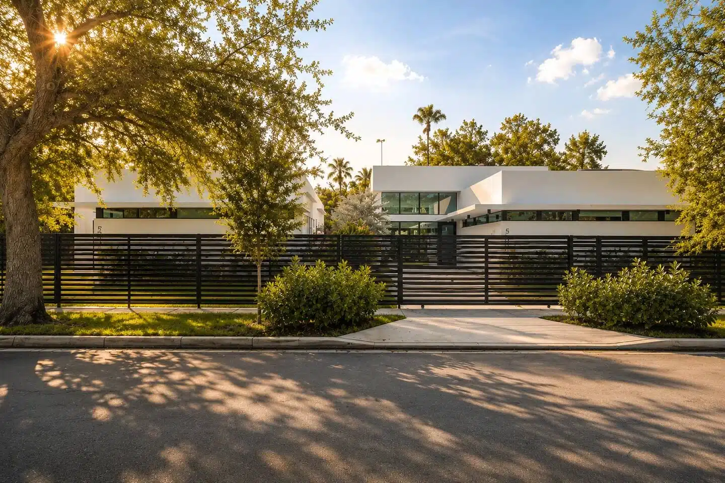Modern white cubic home exterior with black metal fencing and mature trees in Miami, FL