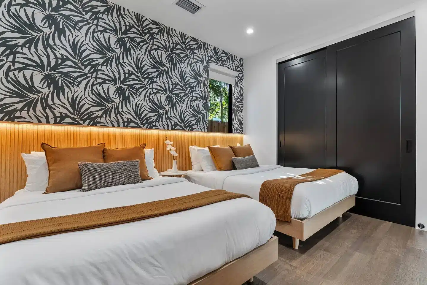 Modern Miami condo bedroom with dual queen beds, botanical wallpaper, and warm lighting