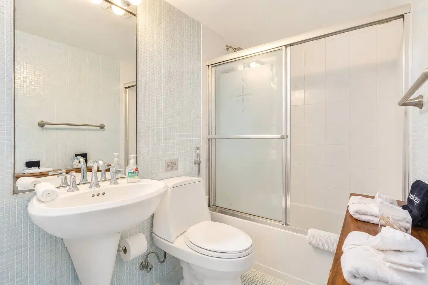 Bright modern bathroom with subway tile, pedestal sink, glass shower enclosure in a Miami Beach group rental for a