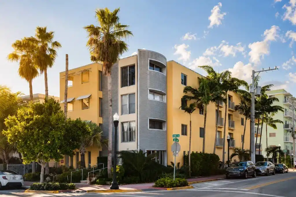 Beachfront beach vacation FL building with curved metallic facade tower, yellow adjacent structures and palm trees in our