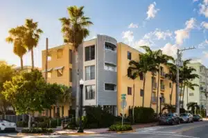 Beachfront beach vacation FL building with curved metallic facade tower, yellow adjacent structures and palm trees in our