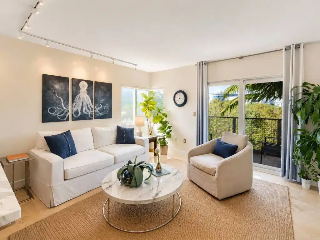 Modern living room with cream sectional, navy pillows, marble coffee table and balcony view in a Miami short term rental by