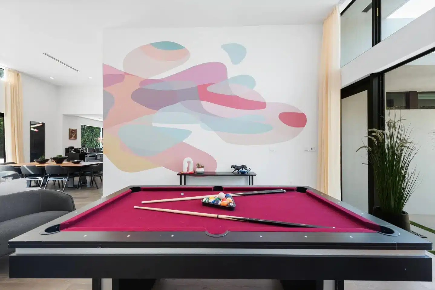Pink pool table with cues beneath a pastel abstract mural in a modern recreation room, a Wynwood-inspired afternoon outing