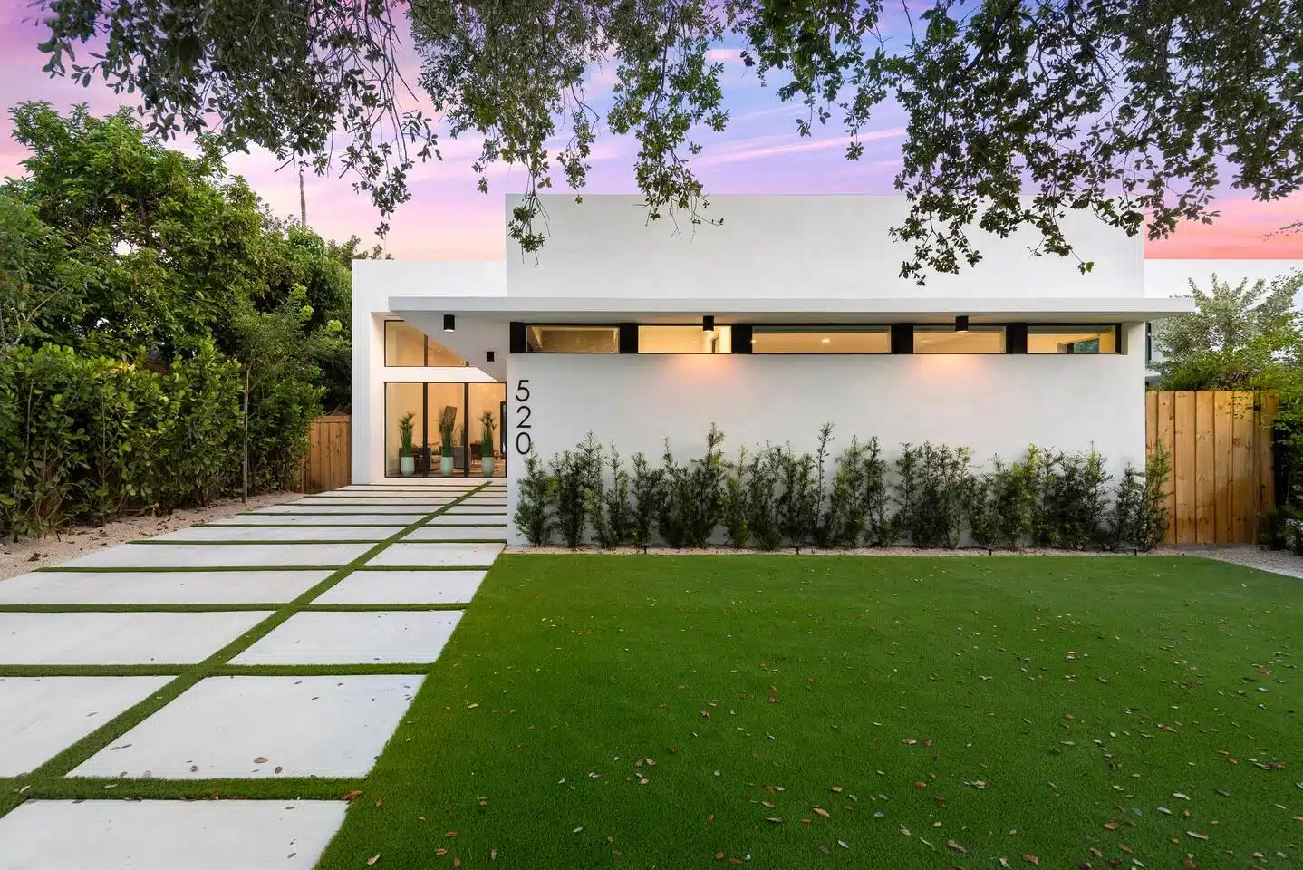 Modern white home with topiary hedges on tree-lined Miami street at sunset