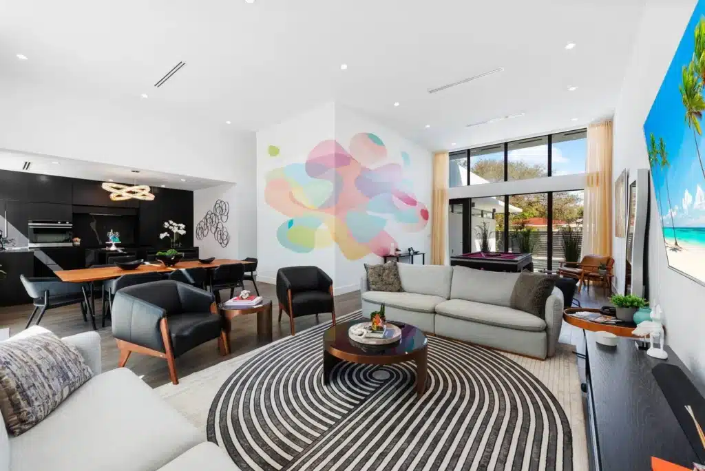 Open-concept living room with abstract colorful mural and floor-to-ceiling windows overlooking a quiet beach morning view in