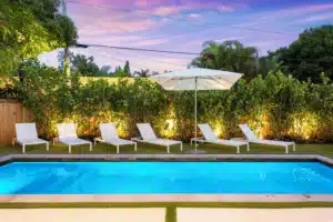 Backyard pool at dusk with crystal-blue water, six white lounge chairs, and palm trees in a 1430 Miami, FL private pool